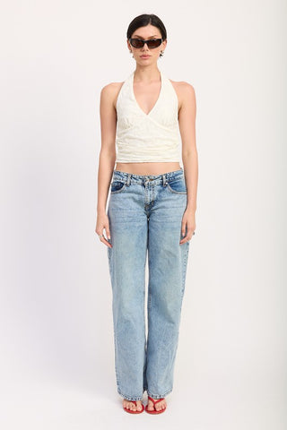 three quarter front view cream lace halter crop top showing crossover V neckline wrap and ruched waist against denim