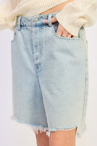 close up detail light blue denim bermuda shorts showing distressed frayed raw hem and denim texture at knee length