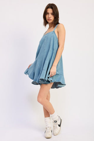 three quarter view light wash denim paneled overall dress showing A-line silhouette and ruffle flared hem panels