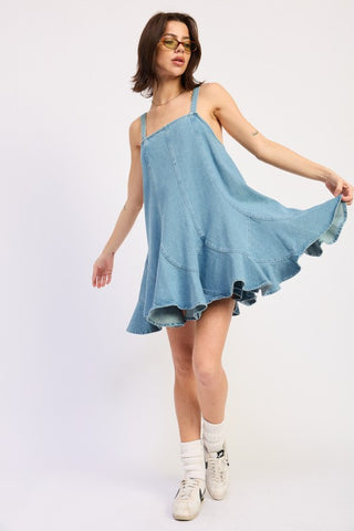 side profile model in light wash denim paneled overall dress showing A-line mini silhouette and ruffle hem flare