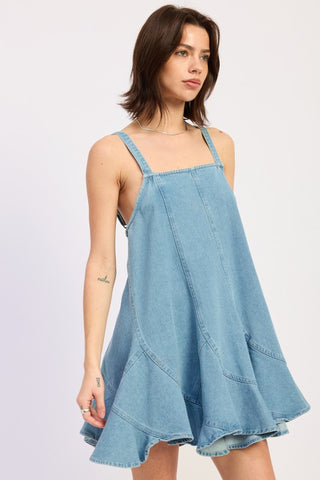 portrait close up model in light blue denim overall dress showing square neckline thick straps and panel construction