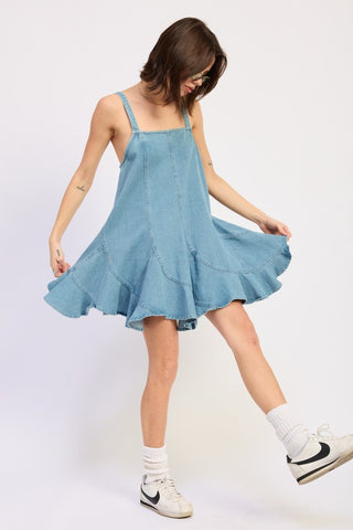 editorial pose model in Penny light wash denim paneled overall sundress showing ruffle hem and A-line silhouette