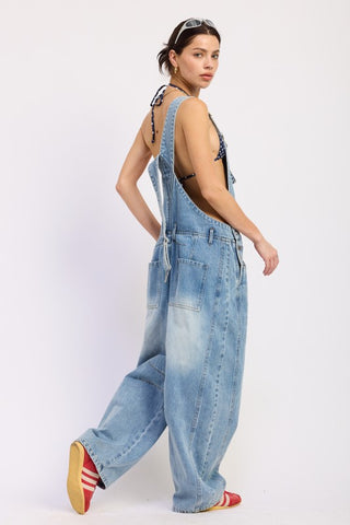 back view model in Nova denim barrel overall showing deep open low back crossed straps and back patch pockets