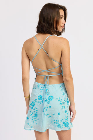 Woman wearing a light blue sequin floral dress with criss-cross back design on a white background