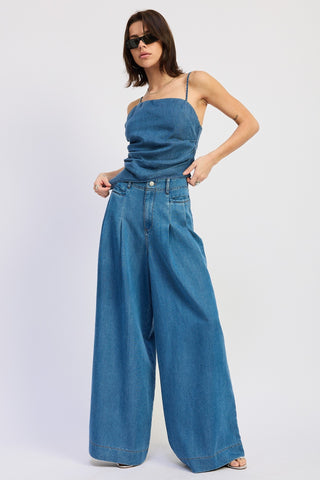 Woman wearing a blue strap top and wide-leg jeans on a white background