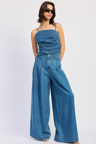 Woman wearing a blue denim outfit with wide-leg pants on a white background