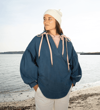 Person wearing a blue oversized hoodie with pink drawstrings on a beach.
